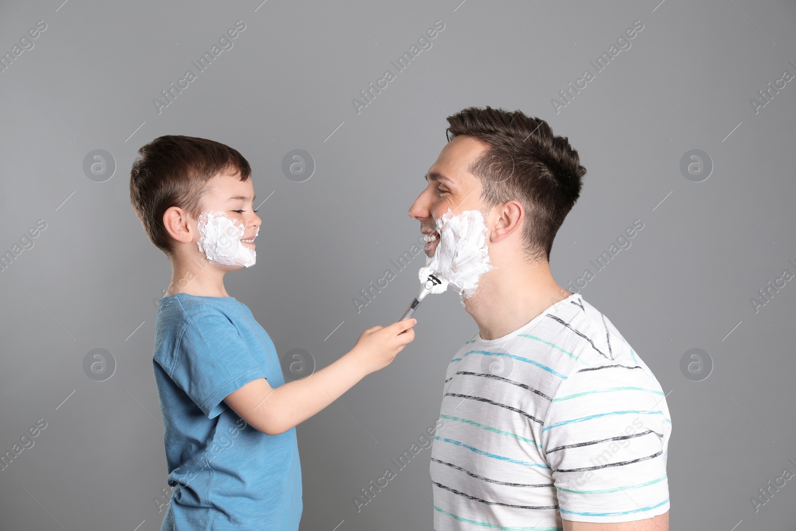 Photo of Little son shaving his father on color background