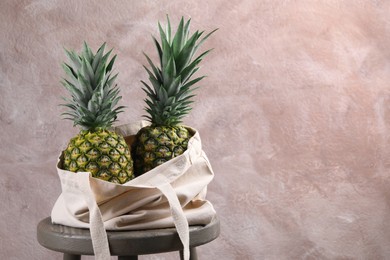 Photo of Bag with delicious ripe pineapples on stand against pink wall. Space for text