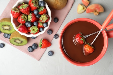 Photo of Dipping strawberries into fondue pot with chocolate on grey table, top view