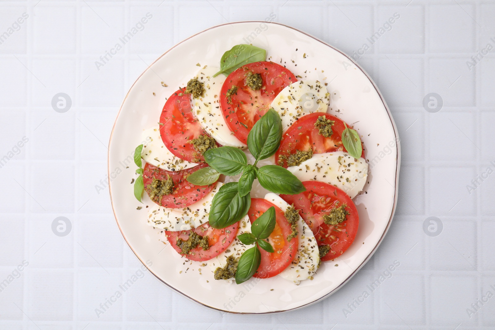 Photo of Plate of delicious Caprese salad with herbs on white tiled table, top view