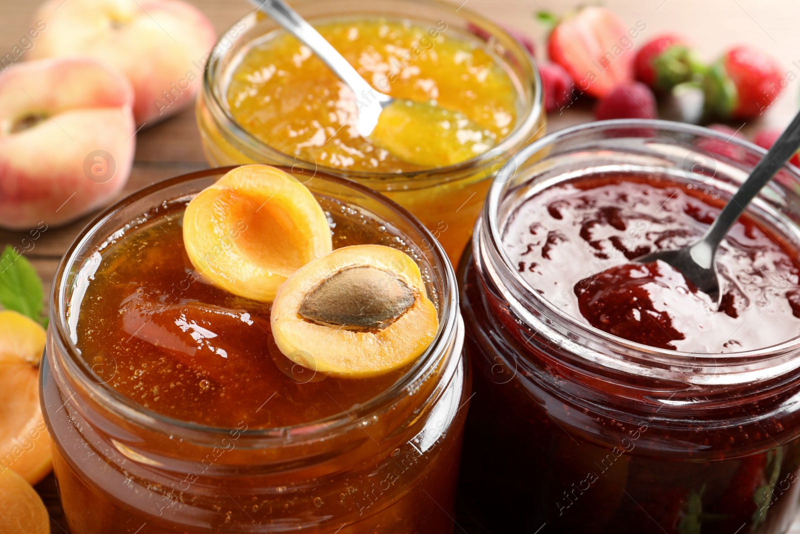 Photo of Jars with different jams and fresh fruits on table, closeup