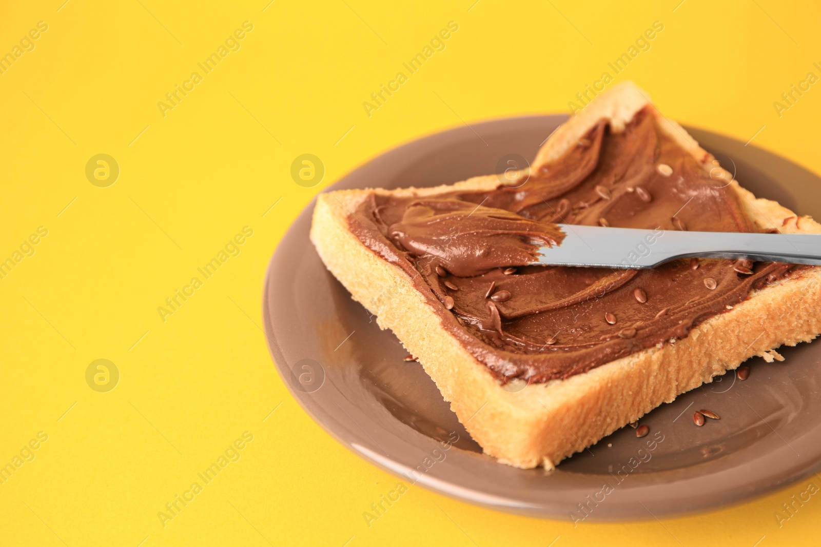 Photo of Spreading chocolate paste onto bread on yellow background, space for text