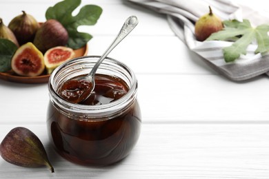 Photo of Jar of tasty sweet jam and fresh figs on white wooden table. Space for text