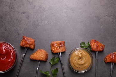 Photo of Fondue forks with pieces of fried meat and sauces on grey table, flat lay. Space for text