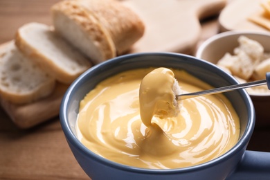 Dipping bread into pot with cheese fondue on table, closeup