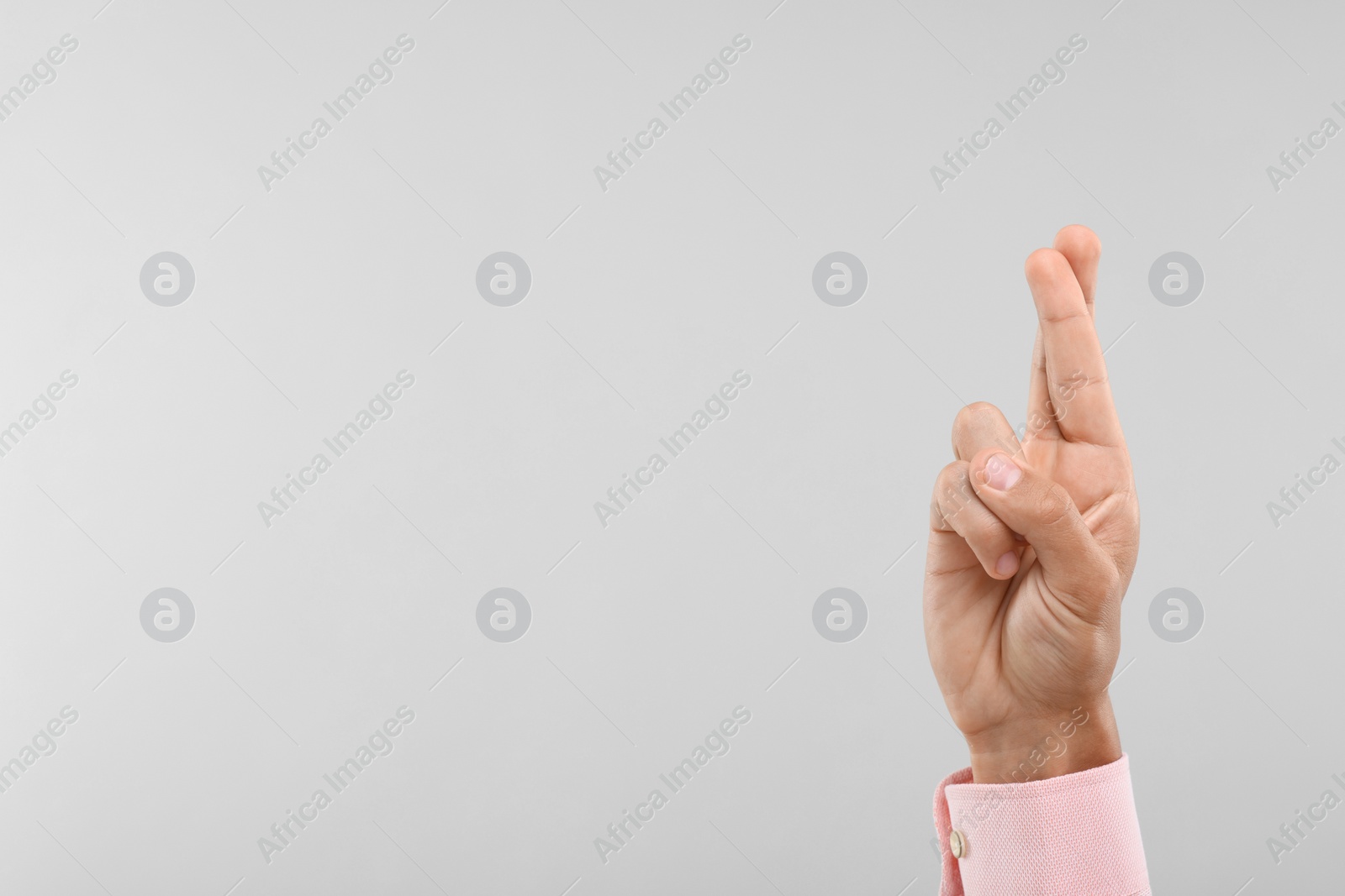 Photo of Young man crossing his fingers on light grey background, closeup. Space for text