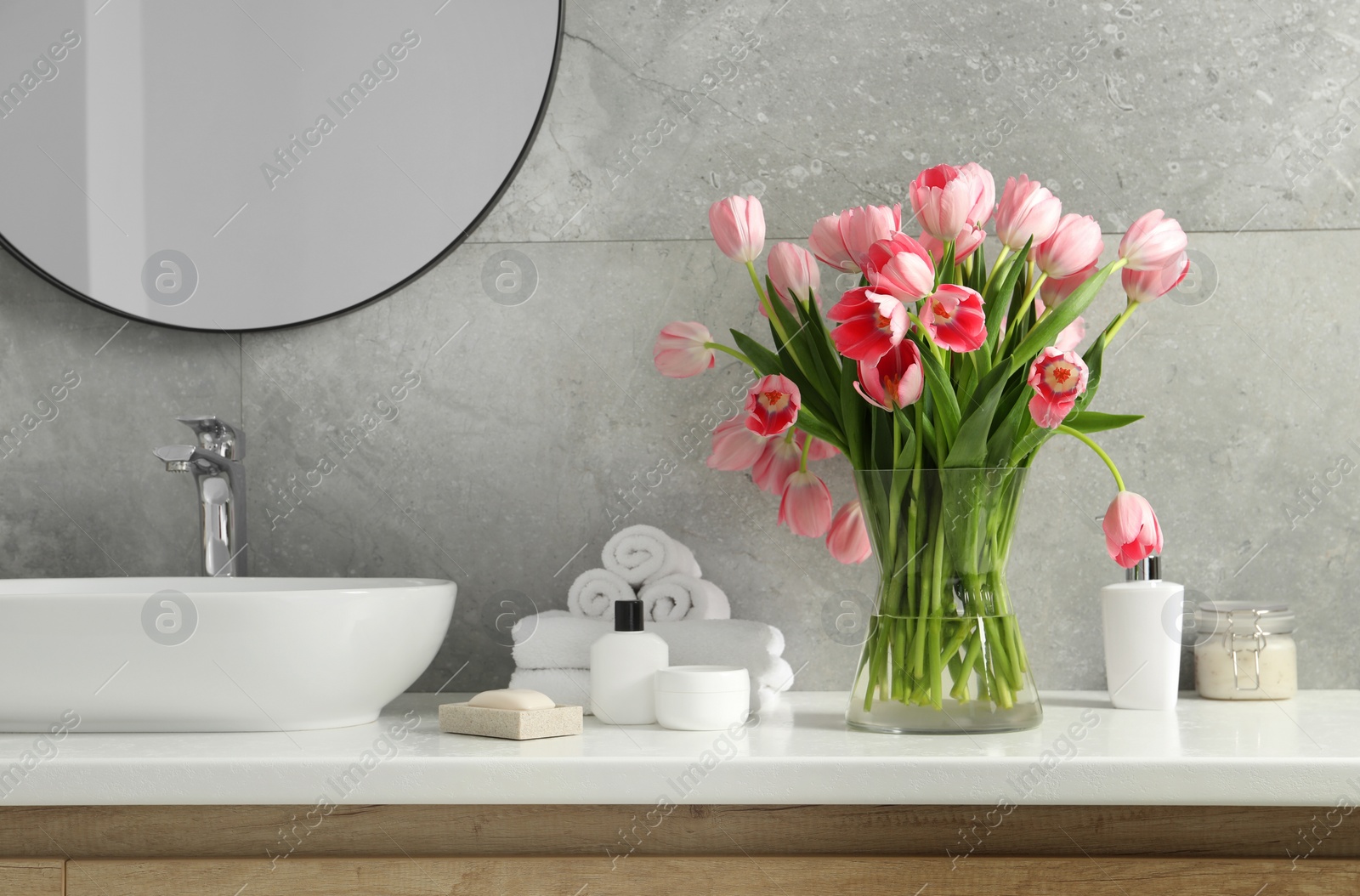 Photo of Vase with beautiful pink tulips and toiletries near sink in bathroom