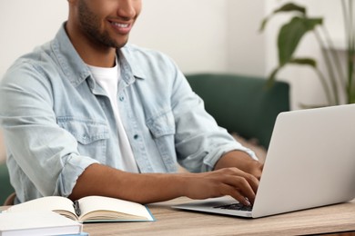 Photo of African American man typing on laptop at wooden table indoors, closeup