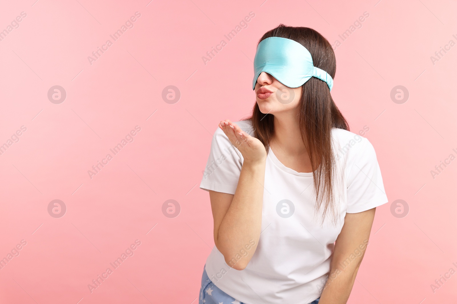 Photo of Woman in pyjama and sleep mask blowing kiss on pink background, space for text