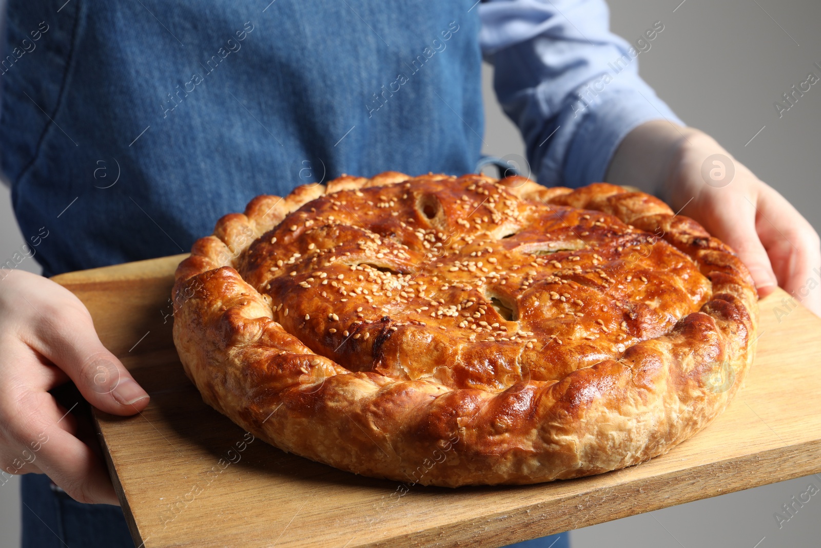 Photo of Woman holding tasty homemade pie on light grey background, closeup