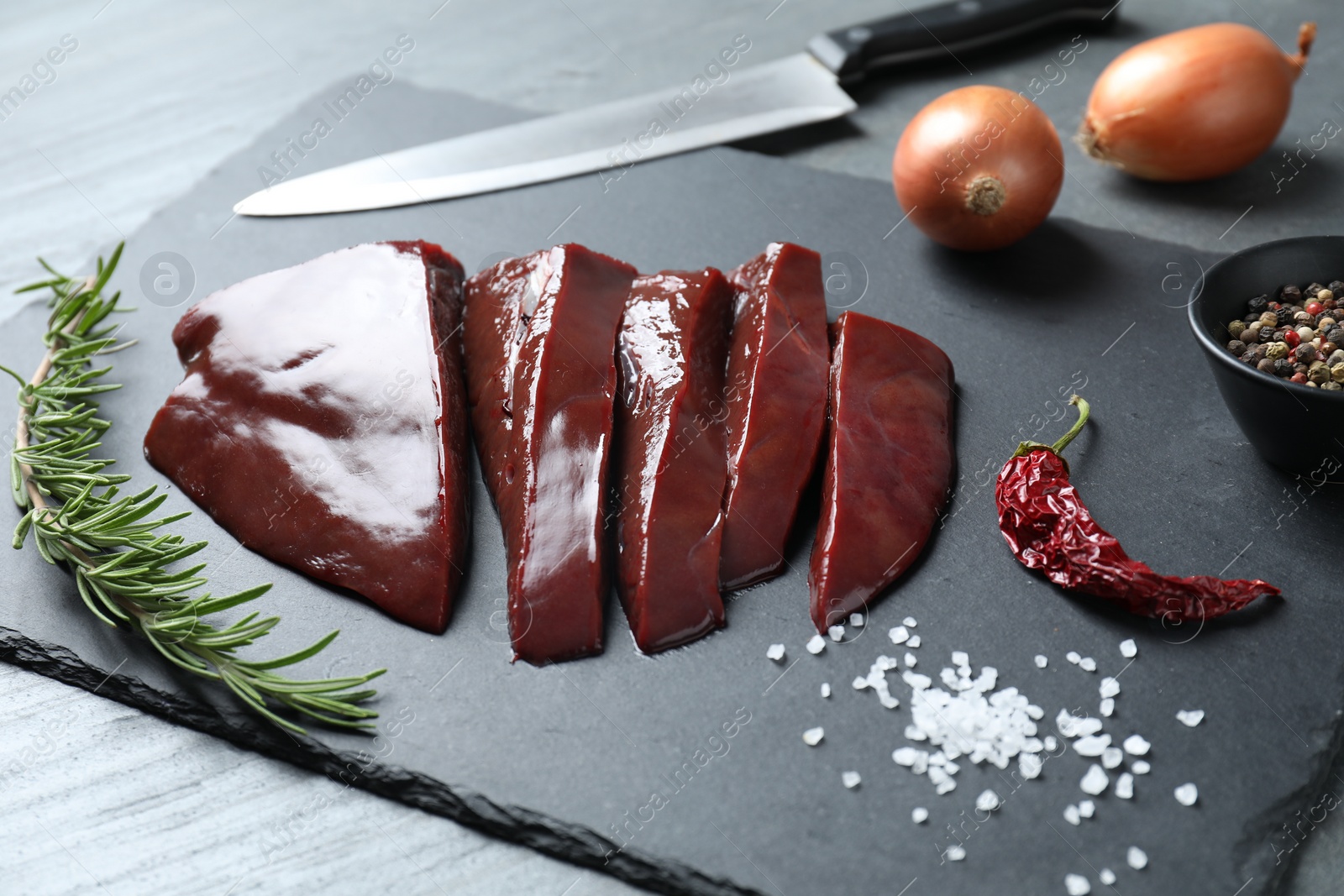 Photo of Cut raw beef liver with rosemary, spices and knife on black table, closeup