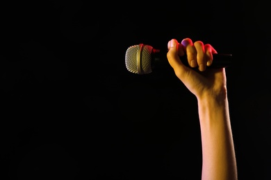 Woman holding microphone on black background, closeup. Space for text