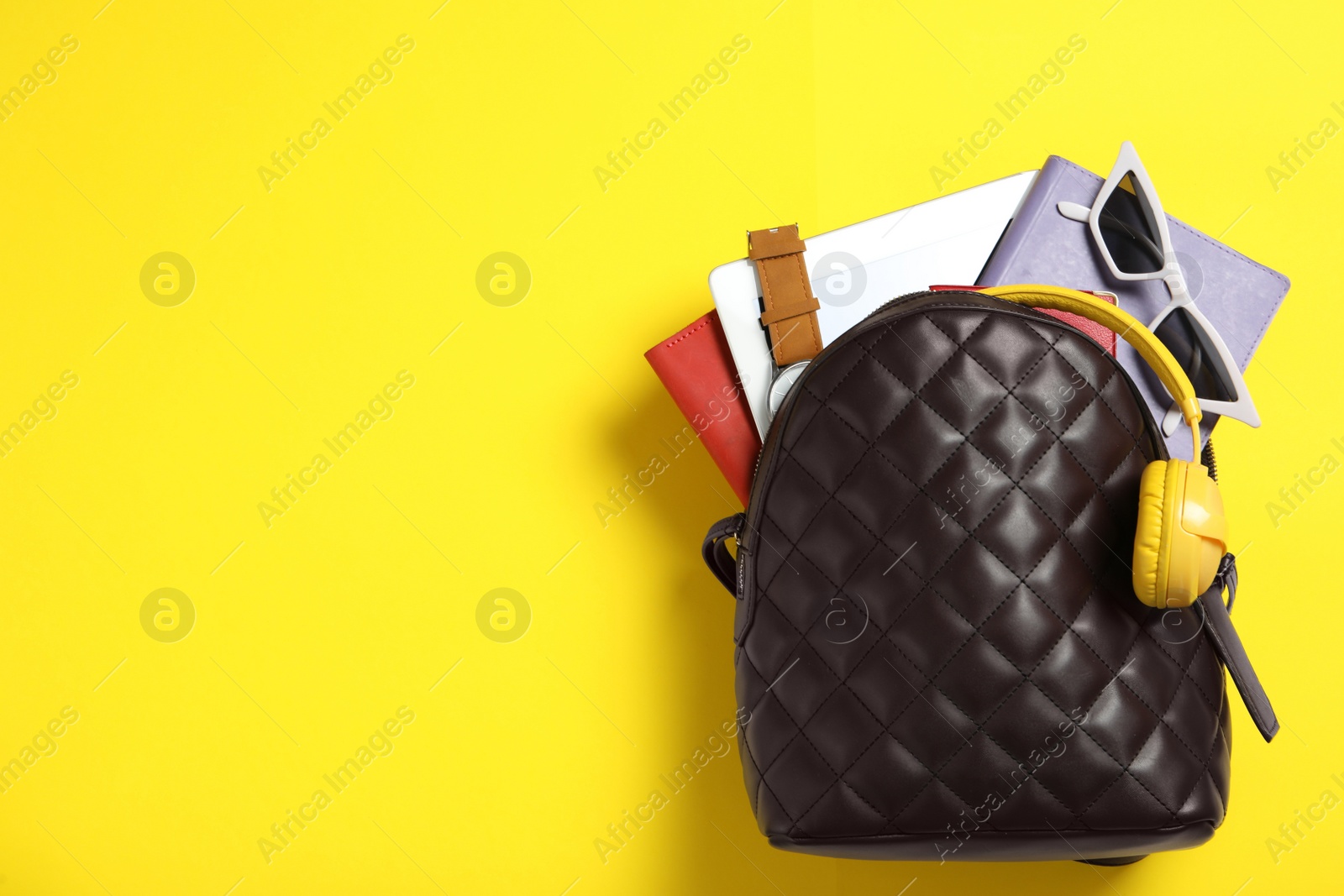 Photo of Stylish urban backpack with different items on yellow background, top view. Space for text