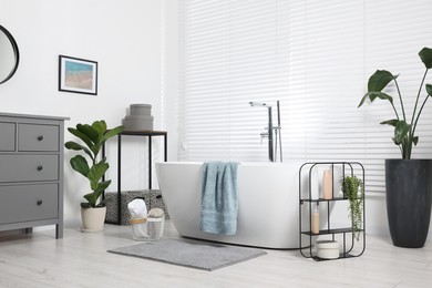 Stylish bathroom interior with bath tub, houseplants and soft light grey mat