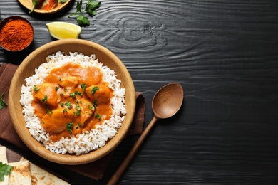 Photo of Delicious butter chicken with rice served on wooden table, flat lay. Space for text