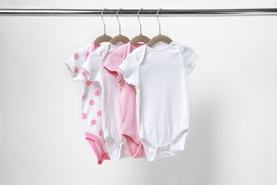 Baby bodysuits hanging on rack near white wall