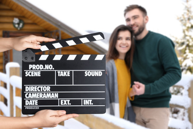 Image of Assistant holding clapperboard and young couple outdoors on snowy day, closeup. Cinema production