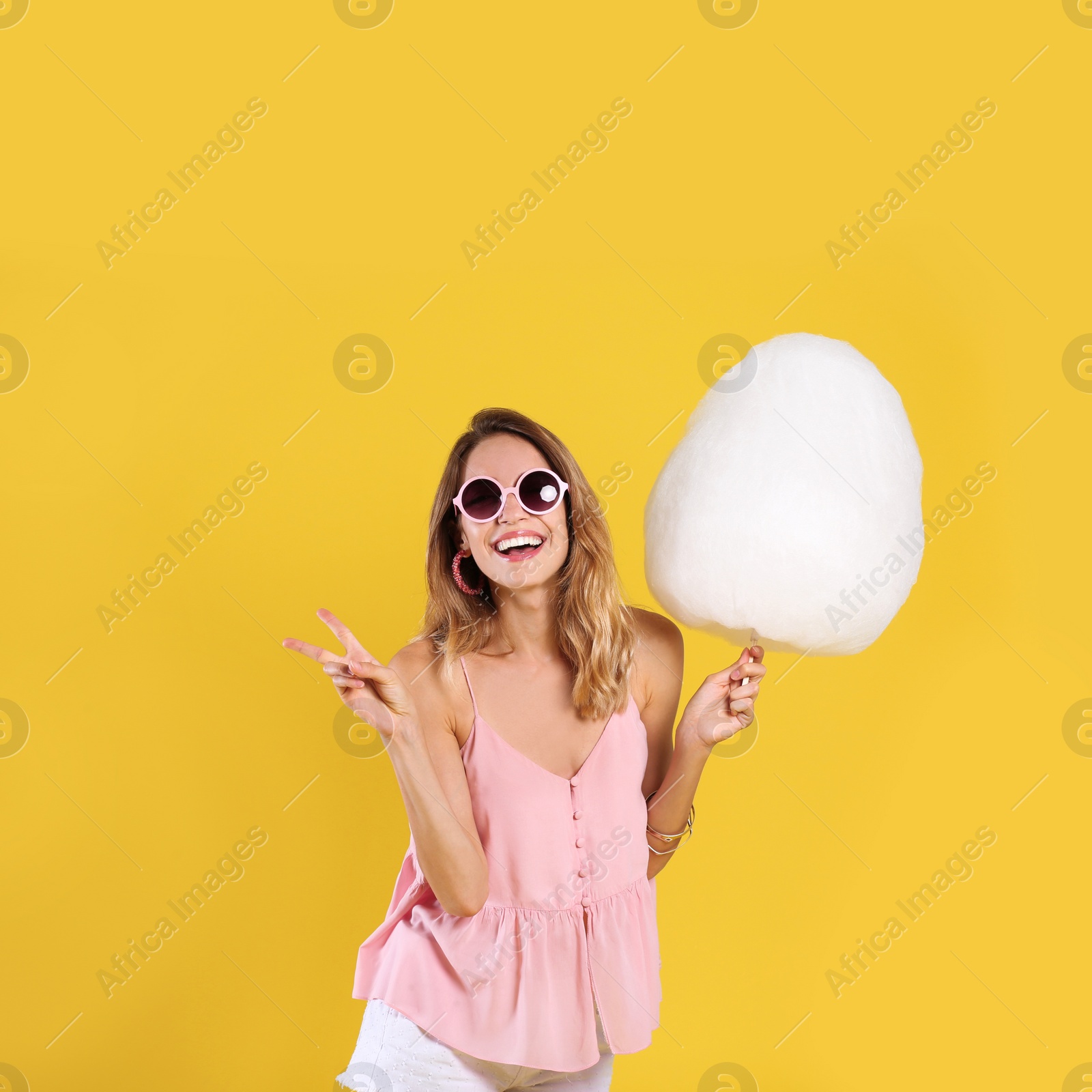 Photo of Happy young woman with cotton candy on yellow background