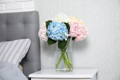 Photo of Beautiful hydrangea flowers in vase on white bedside table indoors