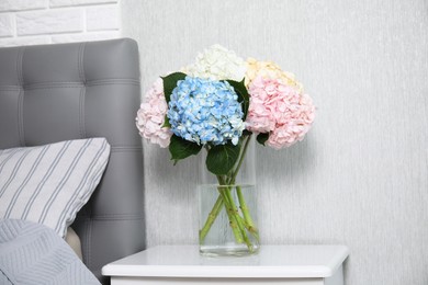 Beautiful hydrangea flowers in vase on white bedside table indoors