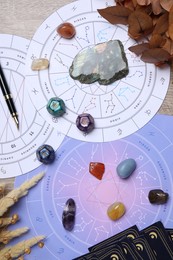 Zodiac wheels, natal chart, astrology dices, fountain pen and gemstones on wooden table, flat lay
