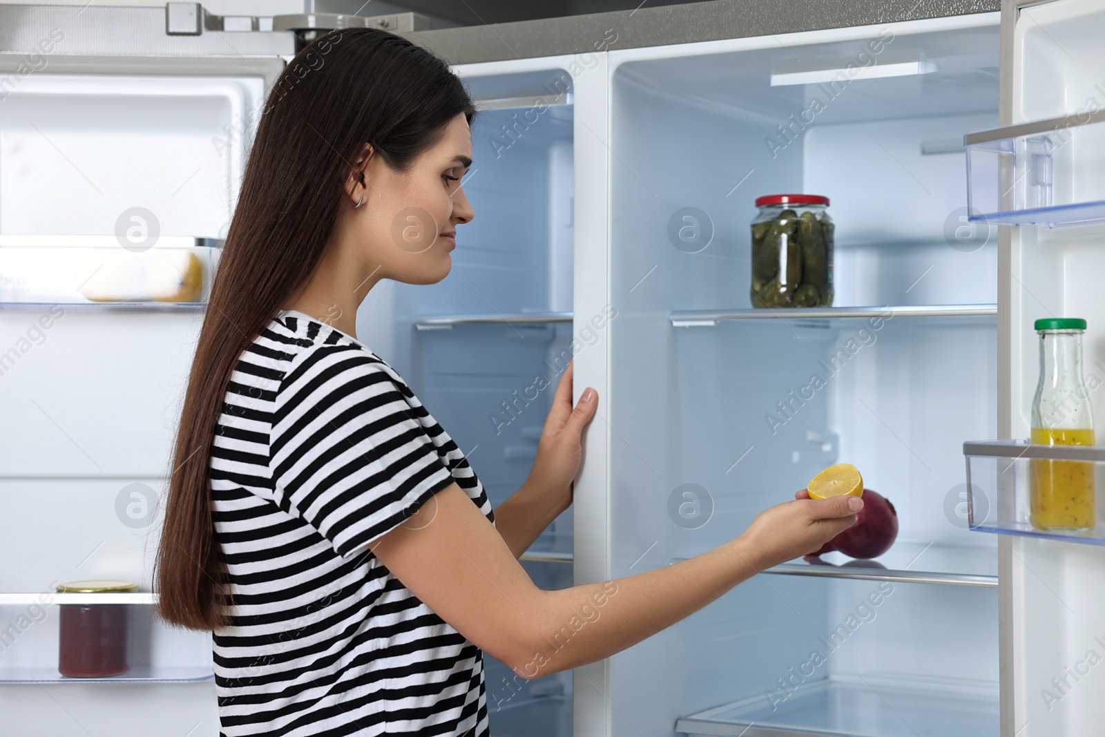Photo of Upset woman taking lemon out of empty refrigerator