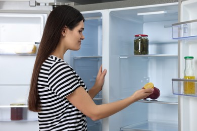 Upset woman taking lemon out of empty refrigerator