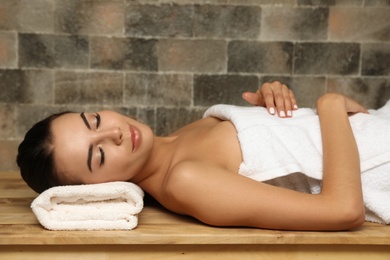 Photo of Young woman lying on wooden bench in salt sauna. Spa treatment