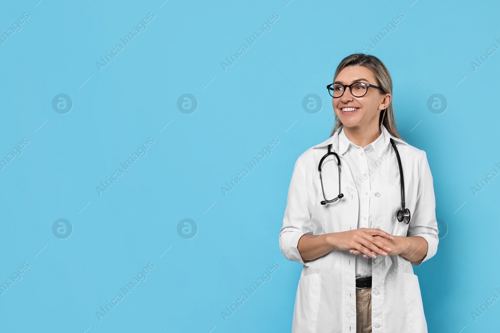 Photo of Portrait of happy doctor with stethoscope on light blue background, space for text