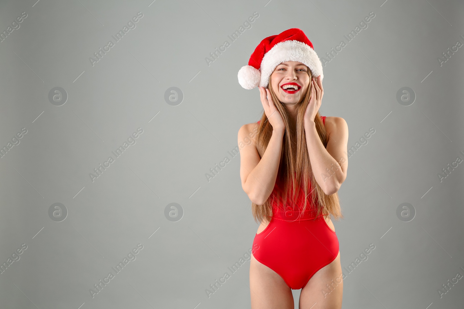 Photo of Young beautiful woman in Santa hat and swimsuit on grey background. Christmas celebration