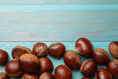 Photo of Roasted edible sweet chestnuts on light blue wooden table, flat lay. Space for text