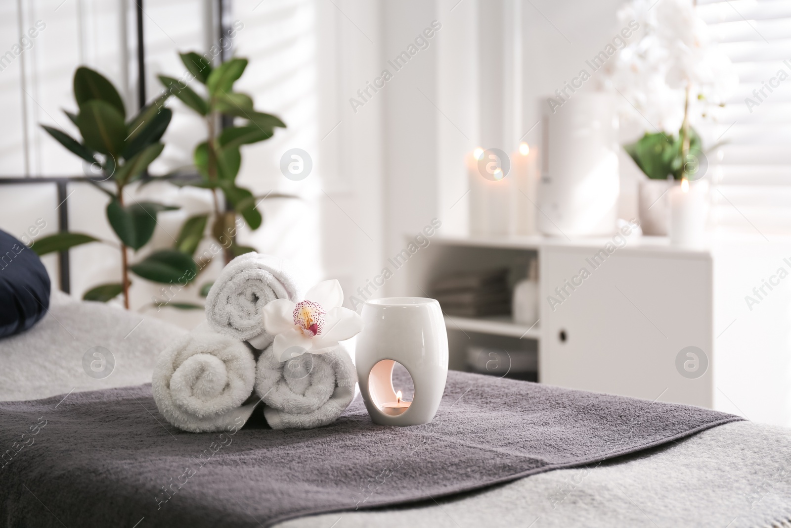 Photo of Towels, aroma lamp and orchid flower on couch in spa salon