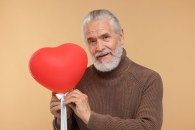 Photo of Senior man with red heart shaped balloon on beige background