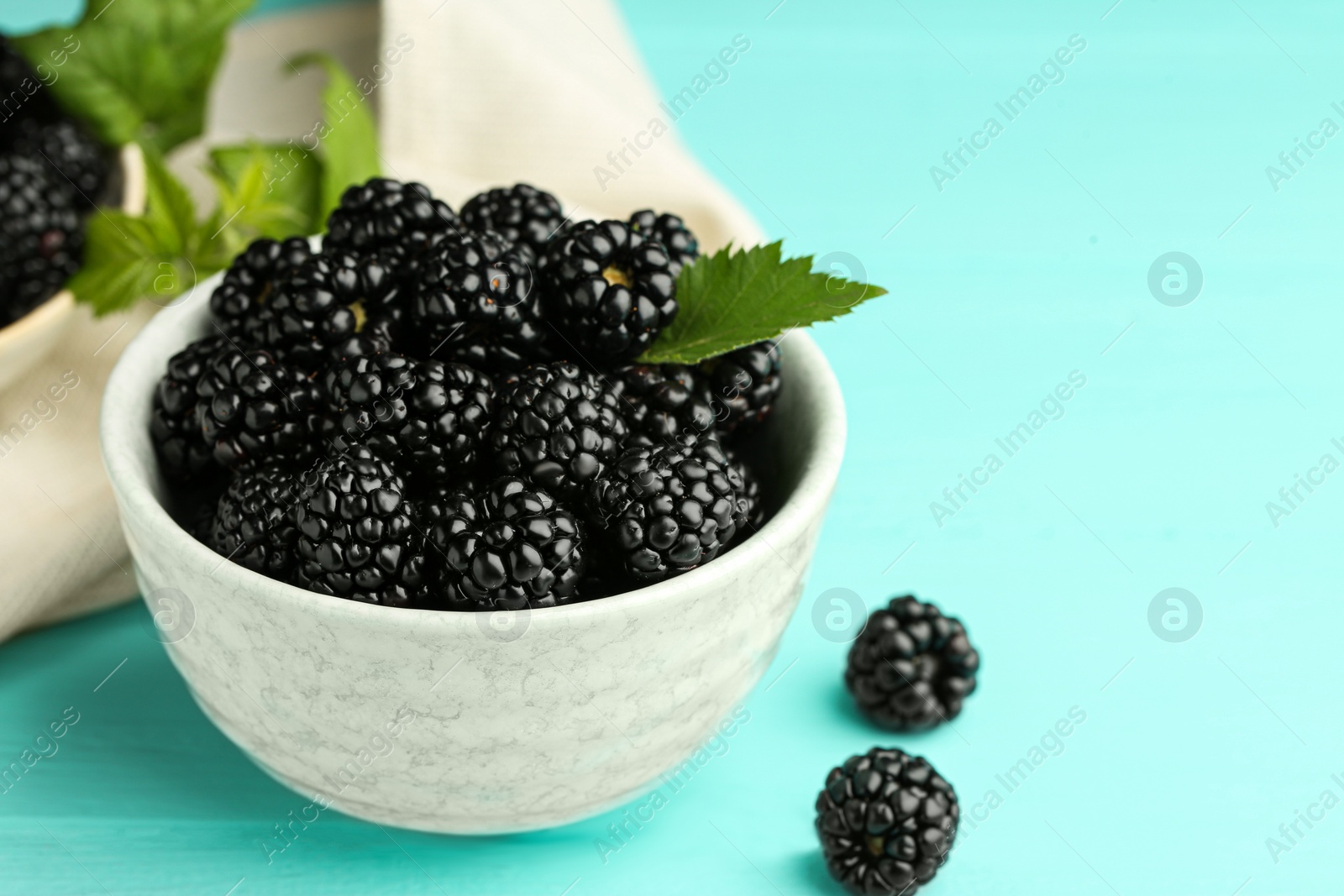 Photo of Bowl of fresh ripe blackberries on turquoise wooden table, closeup. Space for text