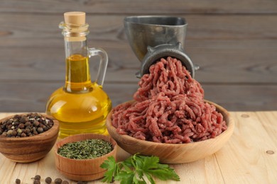 Photo of Mincing beef with manual meat grinder. Parsley, oil and spices on wooden table