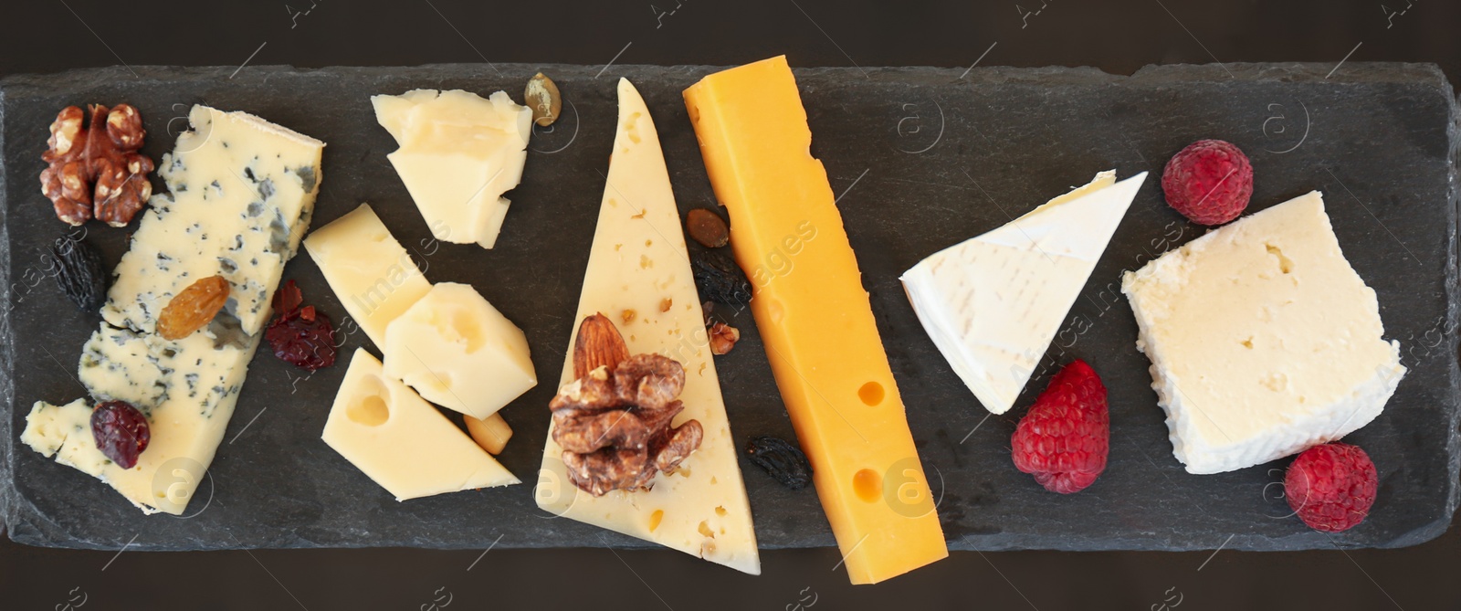 Photo of Different types of delicious cheeses and snacks on slate plate, flat lay