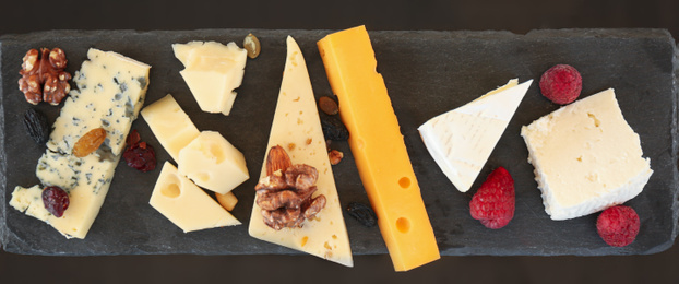 Photo of Different types of delicious cheeses and snacks on slate plate, flat lay