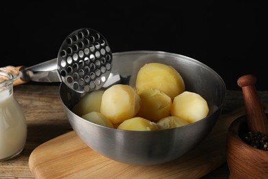 Bowl of tasty boiled potatoes and masher on wooden table