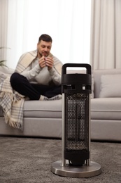 Man with cup of hot drink at home, focus on electric patio heater