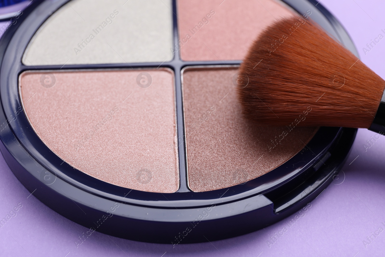 Photo of Colorful contouring palette with brush on violet background, closeup. Professional cosmetic product