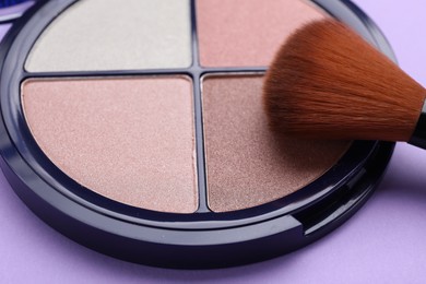 Colorful contouring palette with brush on violet background, closeup. Professional cosmetic product