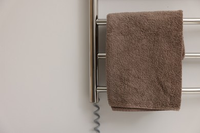 Photo of Heated rail with brown towel on white wall, closeup. Space for text