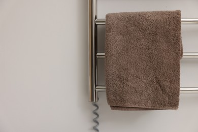 Heated rail with brown towel on white wall, closeup. Space for text