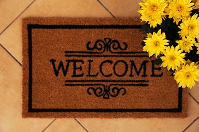 Photo of Door mat with word Welcome and beautiful flowers on floor, flat lay