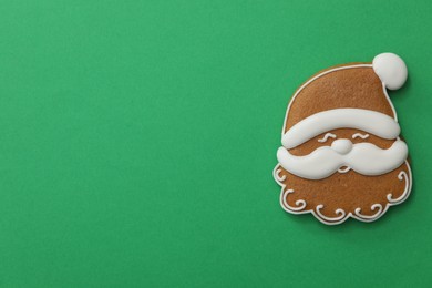 Photo of Christmas Santa Claus face shaped gingerbread cookie on green background, top view. Space for text