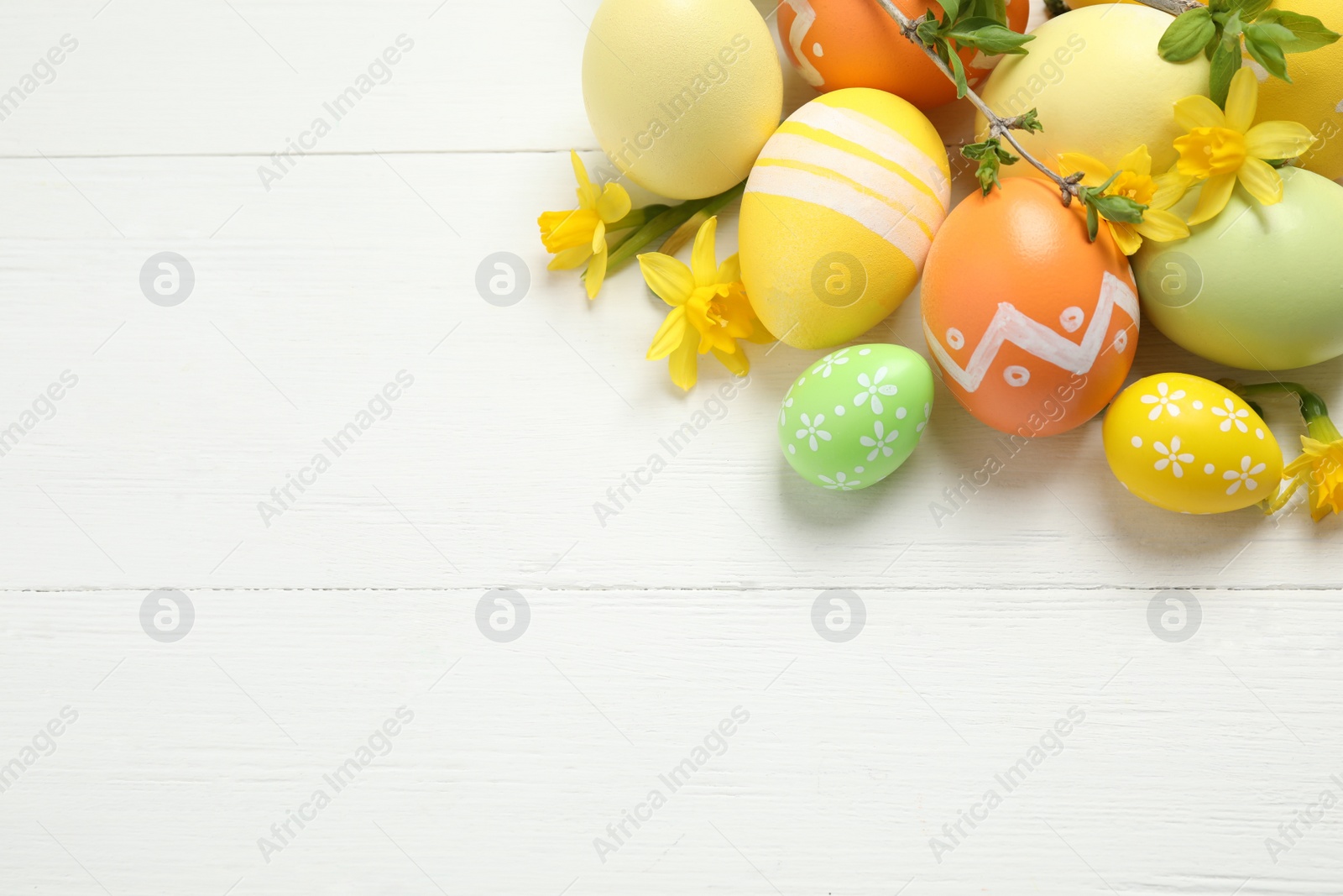 Photo of Colorful Easter eggs and flowers on white wooden table, flat lay. Space for text