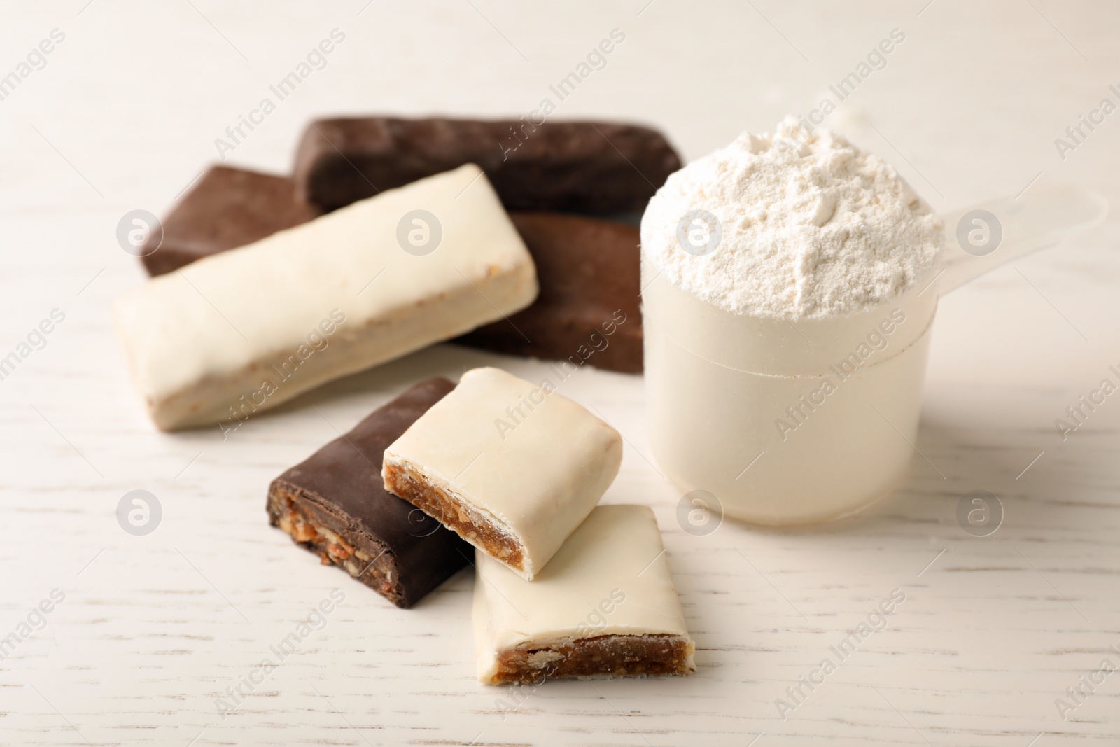 Photo of Tasty protein bars and scoop of powder on white table