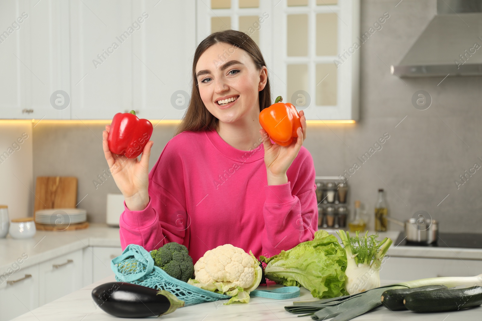 Photo of Woman with peppers and string bag of vegetables at light marble table in kitchen