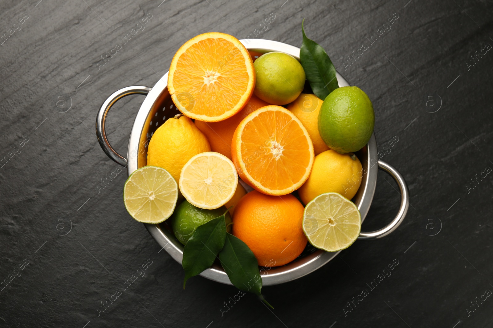 Photo of Fresh citrus fruits in colander on dark textured table, top view