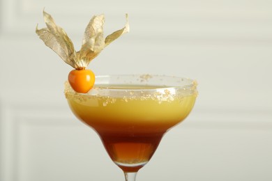 Refreshing cocktail decorated with physalis fruit on light background, closeup